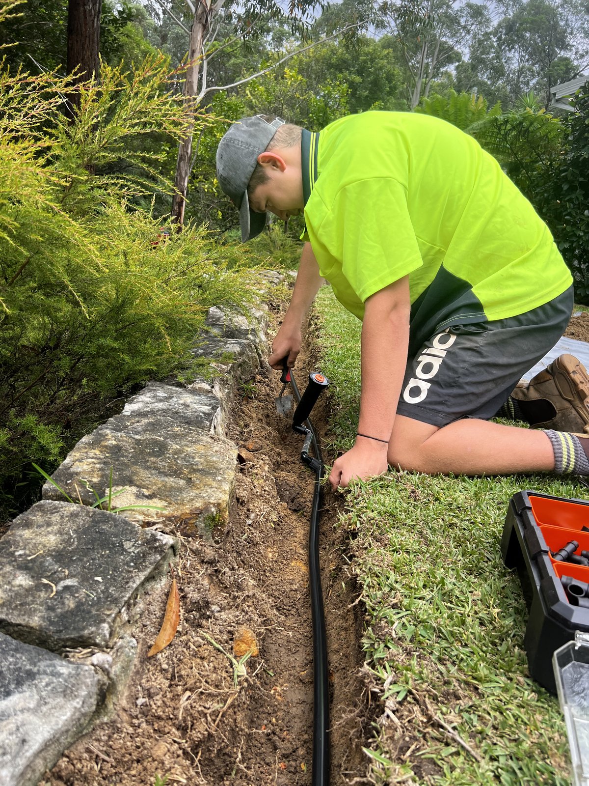 Tradie working on irrigation in stone-walled garden bed